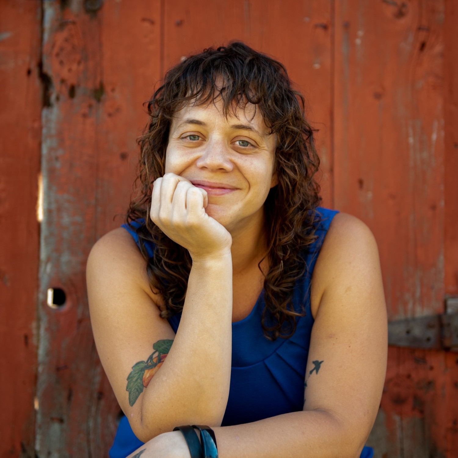 McKenzie Jones, smiling, with hand holding her face, sitting in front of an old wooden red door.